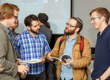 3 students smiling and flipping through the course program at an annual CJS party